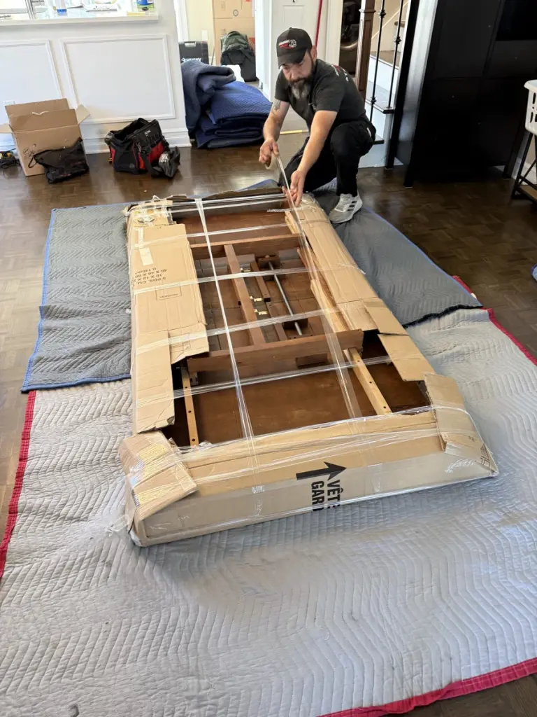 A mover prepares a disassembled piece of furniture on protective moving blankets.