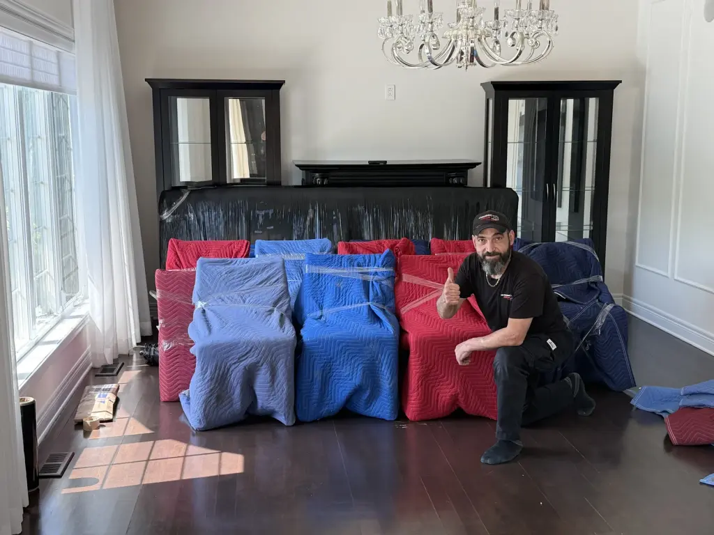 An Arcan team member beside furniture wrapped in red and blue moving blankets.